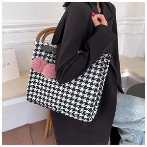 Detail of houndstooth tote bag with pink cherry pendant and black strap on model