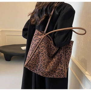 Detail of a large leopard print tote bag with brown leather straps on a black coat