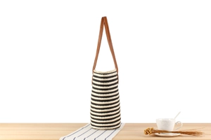 Close-up of woven striped tote bag with leather handles on a minimalist table