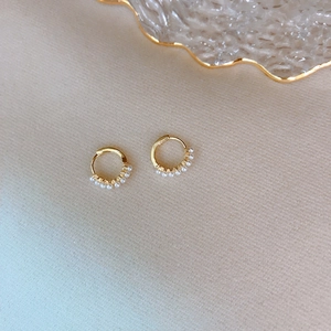Close-up of golden pearl hoop earrings resting on textured beige fabric