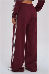 Macro shot of burgundy wide-leg joggers featuring contrast side stripes and elastic high waist