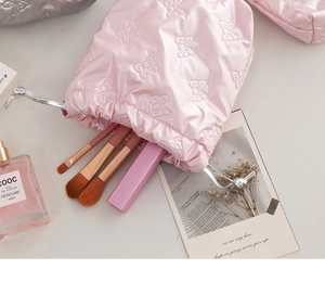 Pink quilted satin drawstring pouch with 3D bow pattern holding makeup brushes
