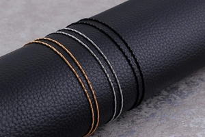Detailed macro view of thin metal cable chains in gold, silver, and black on a black leather stand