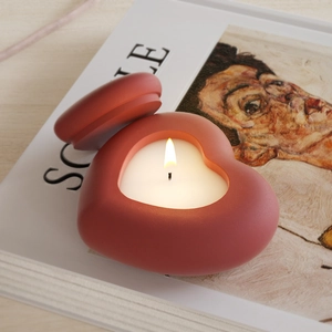 Détail d'une bougie en forme de cœur couleur terre cuite allumée sur un livre blanc