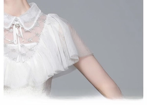 Détail du chemisier en dentelle blanche avec volants délicats et nœud au col