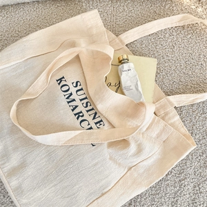 Close-up of cream canvas tote bag with black artistic lettering on textured carpet