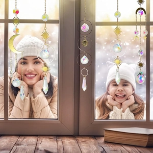 Set of 4 golden crystal suncatchers with moon and star charms hanging by a snowy window