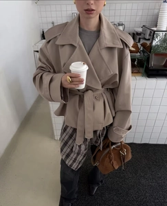 Detail of a beige trench coat with double-breasted buttons and waist belt in a cafe setting