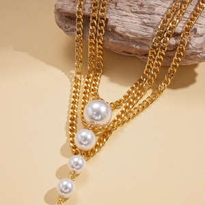 Detailed view of layered gold chain necklace with cascading white pearls on wood base
