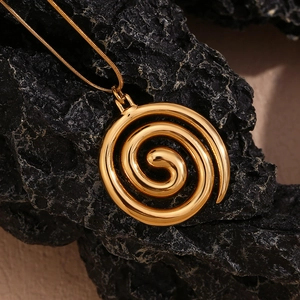 Close-up of golden spiral pendant with delicate snake chain on textured mineral stone