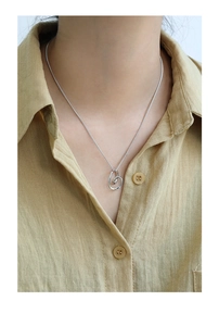 Close-up of S925 sterling silver necklace with abstract heart pendant on linen shirt