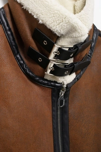 Détail du gilet en daim marron avec col en peau de mouton blanche et passepoil noir