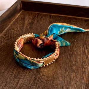 Detail of a gold-toned bangle wrapped with multi-color printed silk and beaded edges