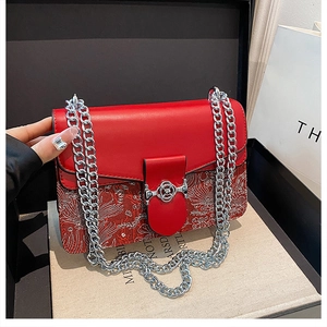 Detailed view of red crossbody bag with silver embroidery and chain strap