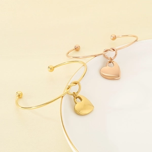Polished gold and rose gold heart pendant knot open bangles on a white ceramic plate