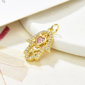 Detail of gold Hamsa pendant featuring a pink heart stone and clear zircon accents