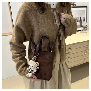 Detail of dark brown suede crossbody bag with a leopard print plush charm accessory
