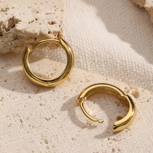 Macro shot of gold S925 sterling silver hoop earrings on a textured stone surface