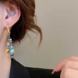 Dettaglio di orecchini lunghi boho con perle turchesi e dorate indossati da modella