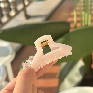 Pink translucent cloud hair claw clip held by hand against a sunny outdoor background