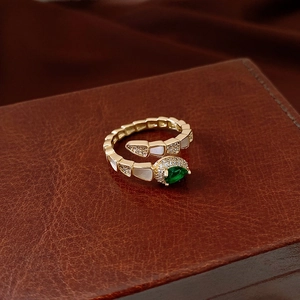 Detailed view of gold snake ring with white shell scales and a green drop gemstone