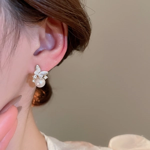 Close-up of butterfly pearl earrings with zircon inlay worn on a female ear