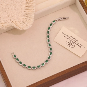 Detail of emerald green zircons on a silver bracelet displayed on a wooden tray
