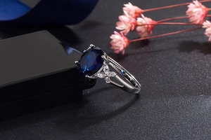 Macro detail of oval blue sapphire ring with small diamonds on black jewelry box