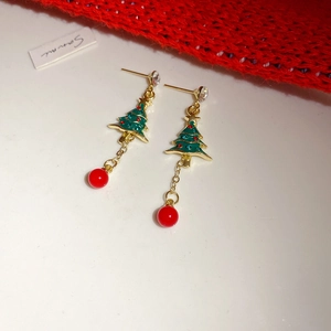 Detail of Christmas tree earrings with green enamel and red beads on a white surface