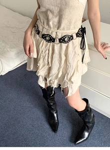 Detail of vintage black leather belt with silver metal rings and rivets over beige skirt