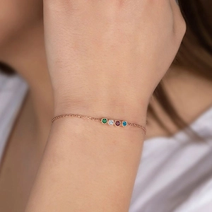 Detail of rose gold bracelet with green, white, red, and blue crystal charms on wrist