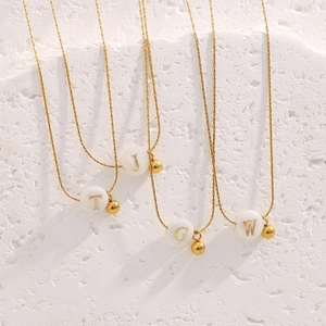 Detail of 18K gold-plated snake chains featuring white initial beads and gold pendants