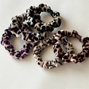 Detailed view of five leopard print velvet hair scrunchies in brown and purple tones