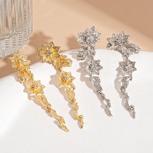 Elegant gold and silver floral drop earrings with rhinestones on a white ceramic plate