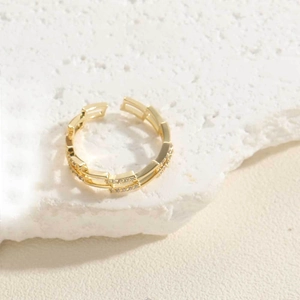 Détails d'une bague chaîne en or sertie de zircons posée sur une surface en pierre