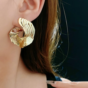 Close-up of a gold chunky earring with a wavy spiral design on a model's ear