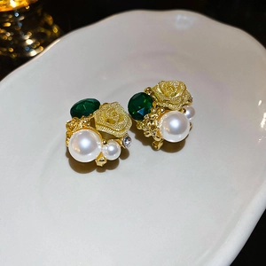 Détail de boucles d'oreilles rose dorée avec cristaux verts et perles sur céramique