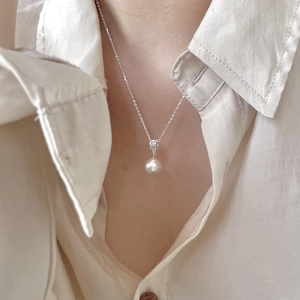 Close-up of elegant pearl pendant with silver chain worn on a minimalist beige shirt