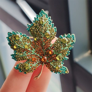 Luxury maple leaf brooch with green and amber crystals on a gold alloy base