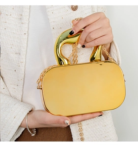 Close-up of golden acrylic mirror box bag with curved metal handle and chain strap