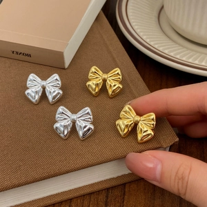Macro detail of gold and silver bow stud earrings showing metallic texture and shine