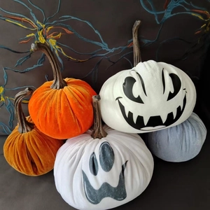 Close-up of velvet Halloween pumpkin pillows in orange and white with spooky face embroidery
