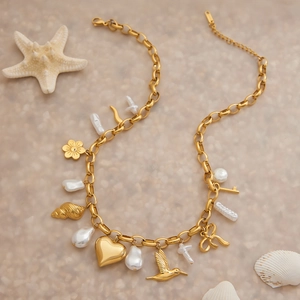 Détail du collier doré en acier inoxydable avec charmes de cœur, oiseau et perle