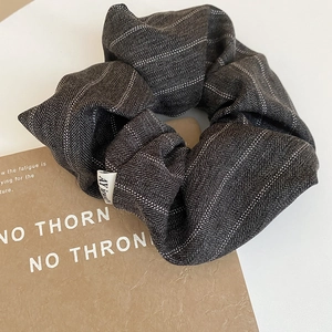 Close-up of a large dark grey herringbone fabric scrunchie with a small white woven label