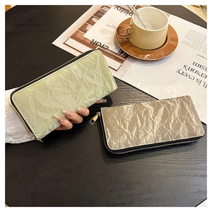 Detailed view of long zip wallets with pleated texture in green and silver grey on a desk