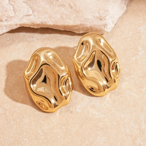 Detailed view of polished gold irregular liquid metal stud earrings on a textured stone