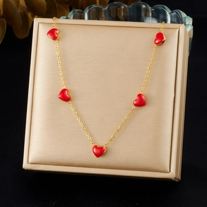 Gold chain necklace with five red heart pendants displayed on a beige jewelry cushion