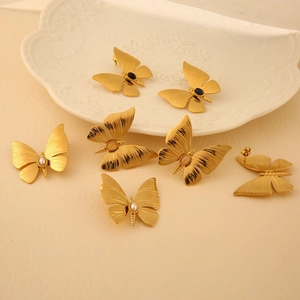 Golden dragonfly stud earrings set with natural stones and pearls on a white plate
