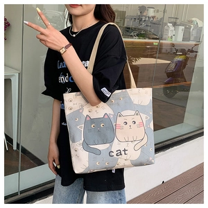 On-shoulder view of a beige canvas tote bag featuring cute cartoon cat prints