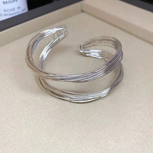 Detail of silver multi-layer twisted open bangle on a minimalist jewelry display tray